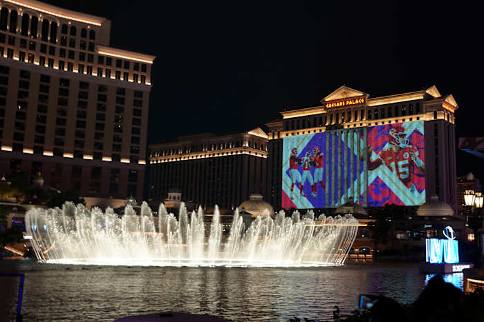Caesar’s Palace in Las Vegas is illuminated with Super Bowl graphics with a fountain in front